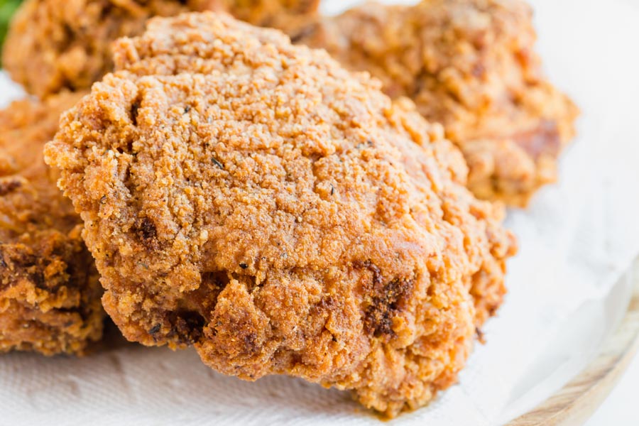 Close up of crunchy fried piece of chicken on a paper towel lined plate.