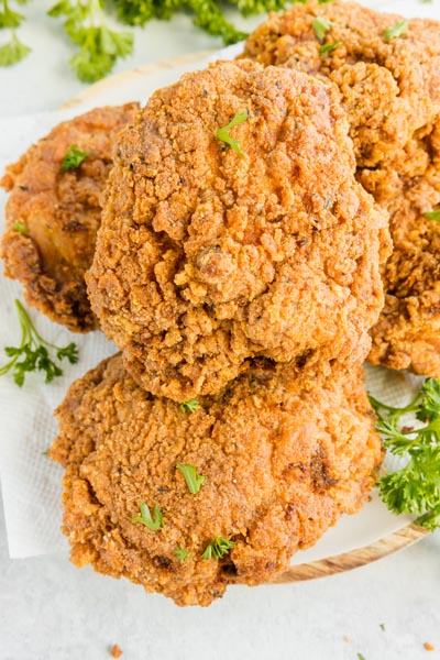 Fried breaded chicken on a plate with crumbs and parsley scattered around.