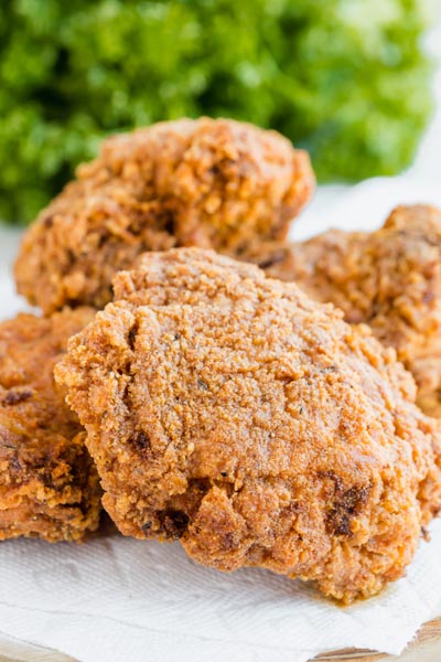 A bunch of fried pieces of chicken on a plate with parsley behind the pile.