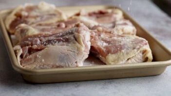 A baking tray with skin on chicken thighs being seasoned with kosher salt.