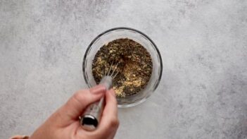 A hand whisking a spice blend in a small bowl.