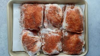 Six pieces of skin on chicken thighs coated with a red seasoning.