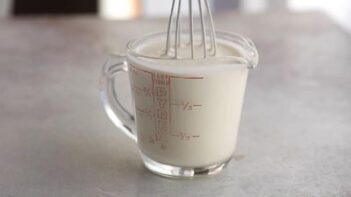 A wire whisk stirring a cream in a measuring cup.