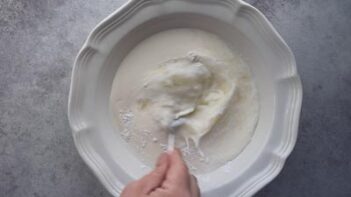 A hand stirring a milk mixture with a fork.