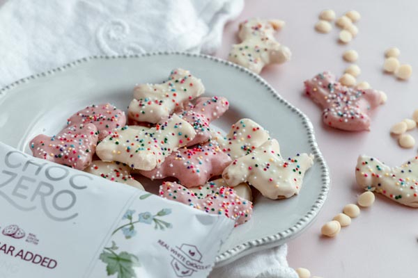 sugar free frosted animal cookies coated with white chocolate and sprinkles on a plate with a bag of choczero chips