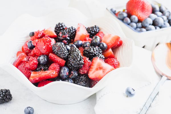 juicy berries in a white scalloped shape bowl with blueberries in the background
