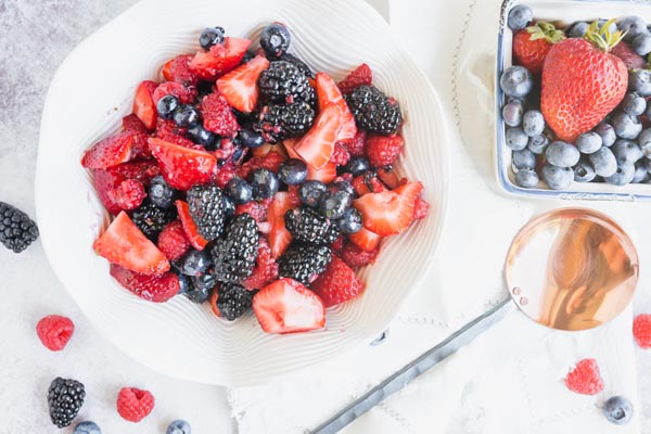 a big bowl of mixed berry salad next to a copper spoon and a carton of berries