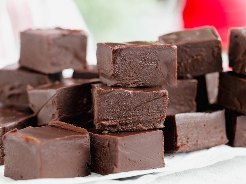 A large pile of smooth, glossy keto chocolate fudge squares arranged on parchment paper.