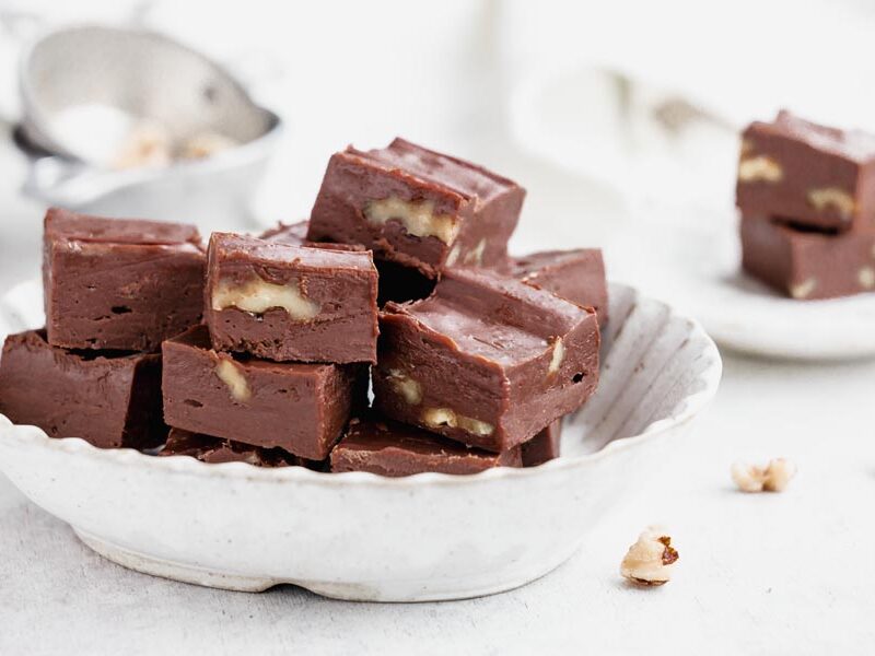 A bowl filled with keto walnut fudge squares stacked neatly with nut pieces showing.