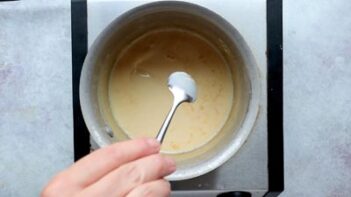 A saucepan of cream, warm butter and sweetener being stirred with a spoon as the mixture melts.