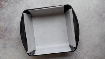 A square baking pan lined neatly with parchment paper for preparing fudge.