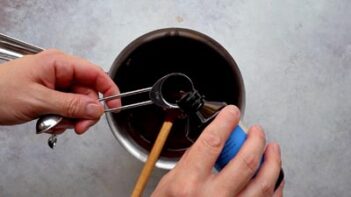 Vanilla extract being measured and poured into a saucepan of melted chocolate mixture.