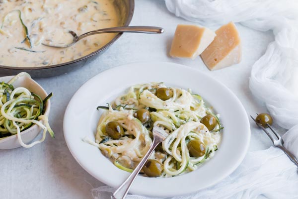 spooning alfredo sauce on zoodle pasta