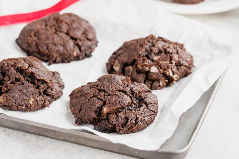 A baking tray with four baked chocolate cookies on top of parchment paper.