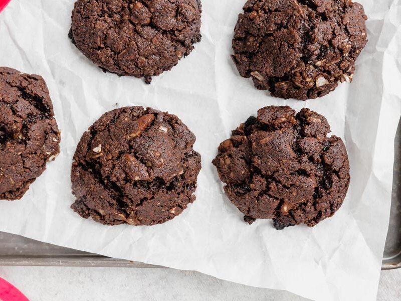 A baking tray lined with parchment paper and five chocolate cookies filled with pecans and coconut on top.