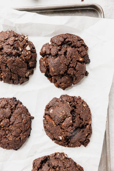 Baked chocolate cookies on a sheet of parchment paper on a baking tray.