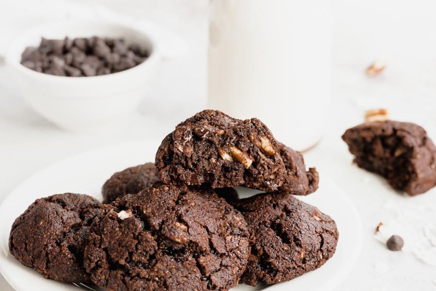 A plate with freshly baked chocolate cookies and a half a cookie on top showing the melted chocolate inside.