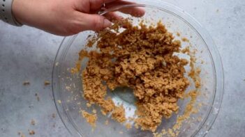 A hand holds a bowl with cookie dough inside.