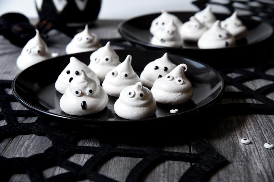 a bunch of halloween cookies on two plates underneath a black spiderweb