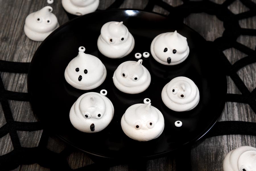 meringue cookies in a shape of ghosts on a plate with candy eyes scattered
