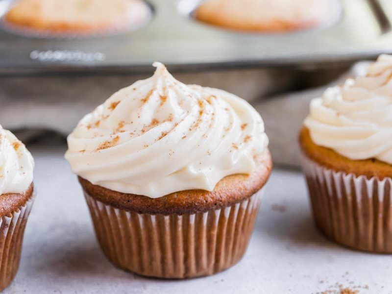three muffins with cream cheese frosting swirled on top and topped with nutmeg