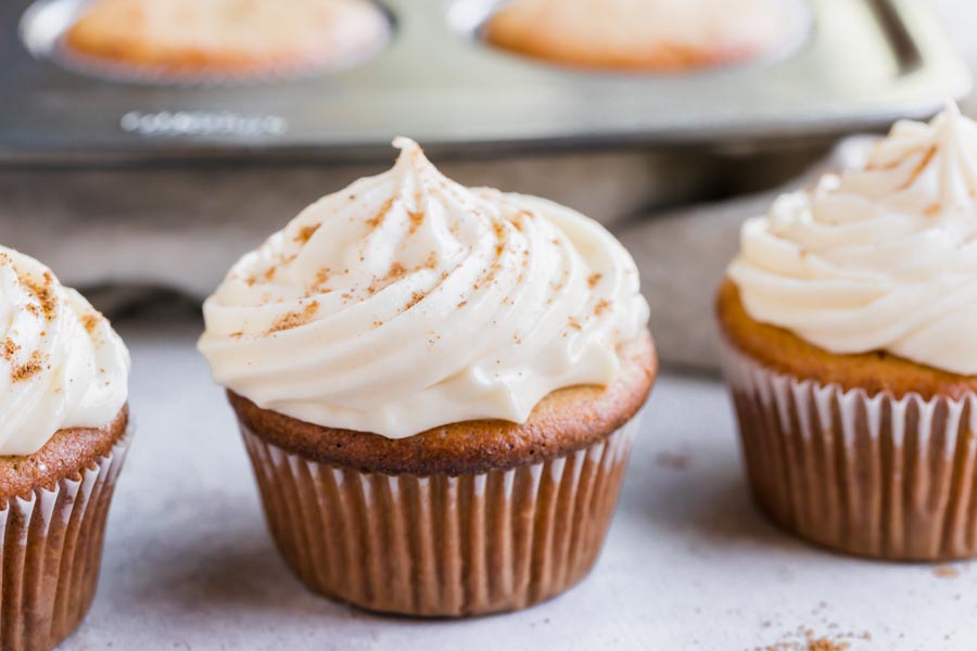 three muffins with cream cheese frosting swirled on top and topped with nutmeg