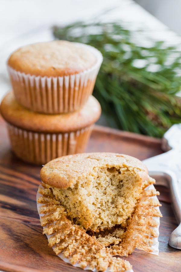 a muffin with a bite taken out of it and the muffin liner pealed back, two muffins stacked behind it