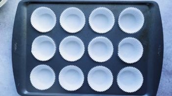 a muffin pan filled with white muffin liners in the cavities