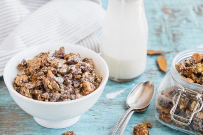 a bowl of keto granola with milk in the back ground and a container of extra granola
