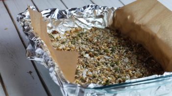 granola mixture pressed in to a baking dish with parchment paper hanging out