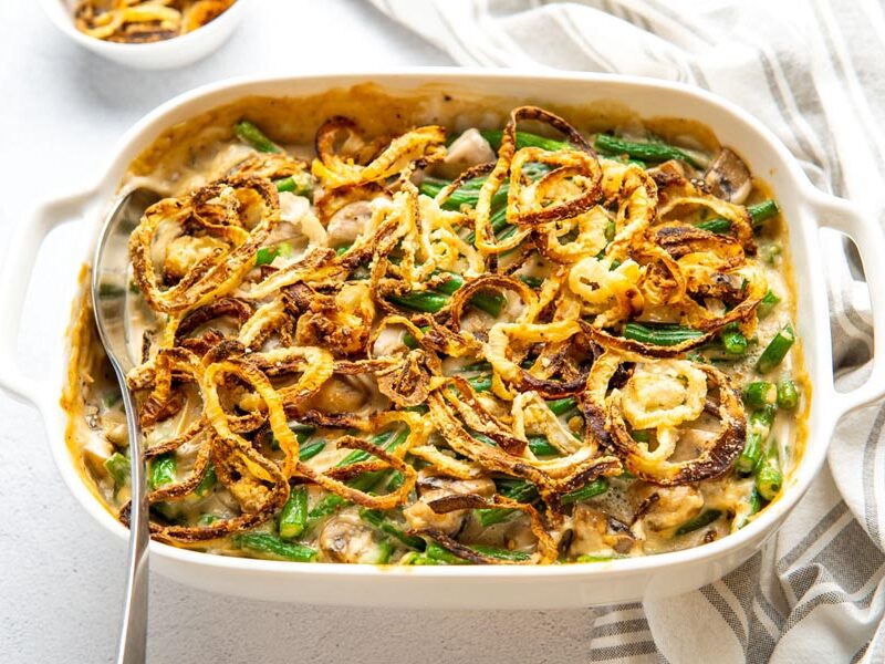 A serving spoon in a casserole filled with green beans and fried onions.