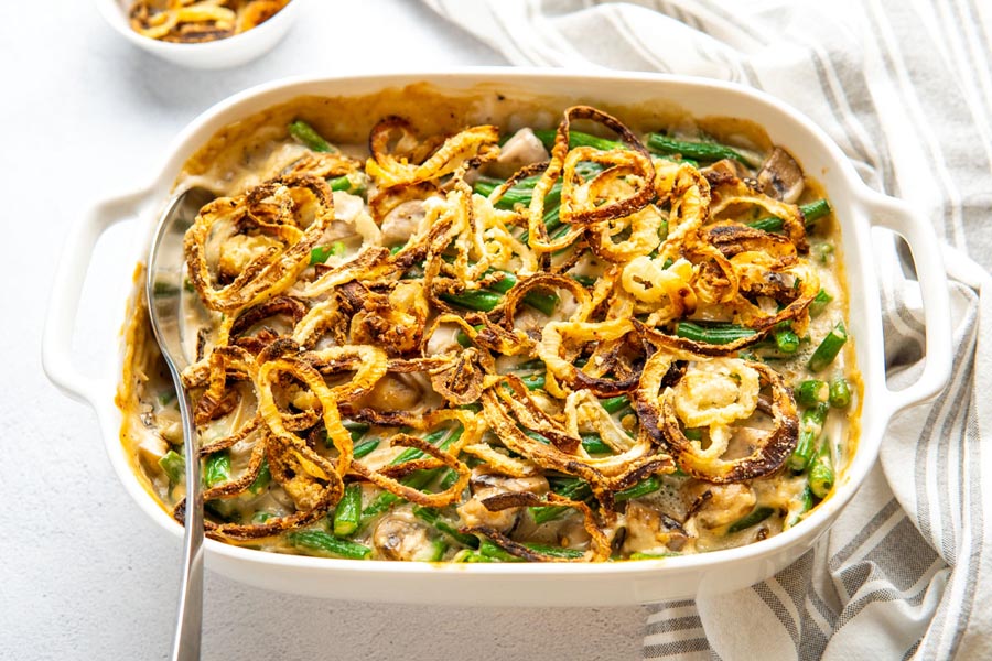A serving spoon in a casserole filled with green beans and fried onions.