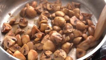 A skillet with quartered mushrooms sautéing.