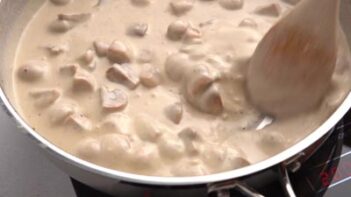 A wood spoon stirring a thick and cream cream of mushroom soup mixture.