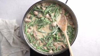 A wooden spoon in a skillet with creamy mushroom and green beans.
