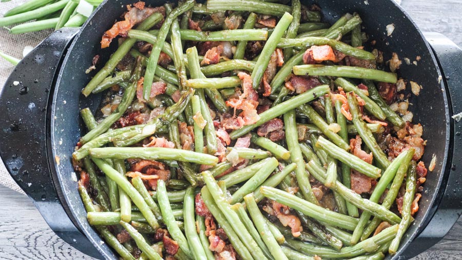 greens beans cooking in a skillet with bacon
