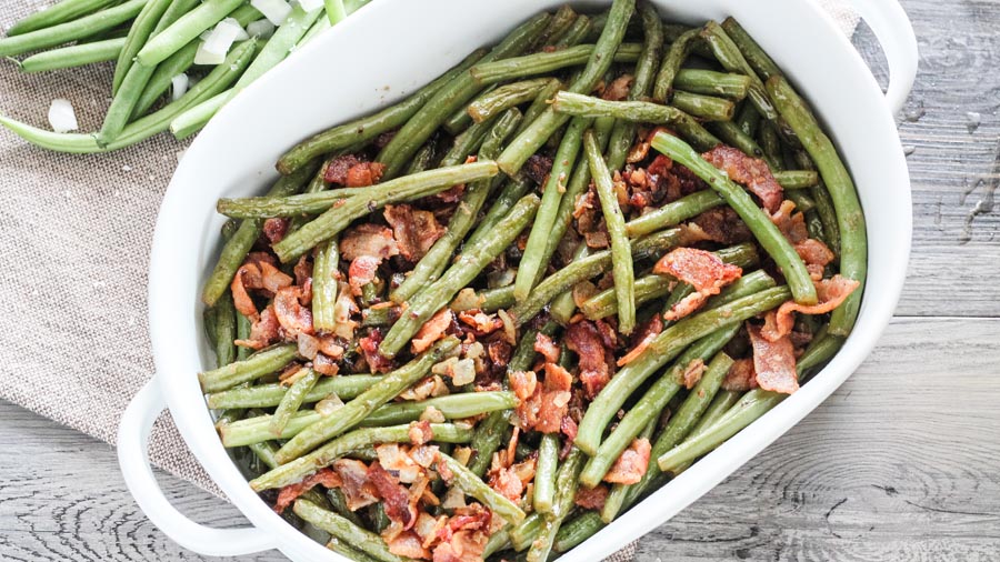 a white dish filled with cooked green beans and bacon