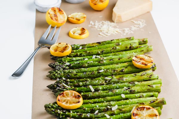 grilled asparagus on a parchment paper with grilled lemons and a fork