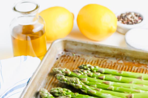 fresh asparagus on a baking tray with olive oil and parmesan cheese nearby