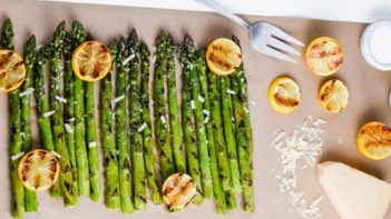 grilled asparagus on a sheet of parchment paper with lemons and parmesan cheese