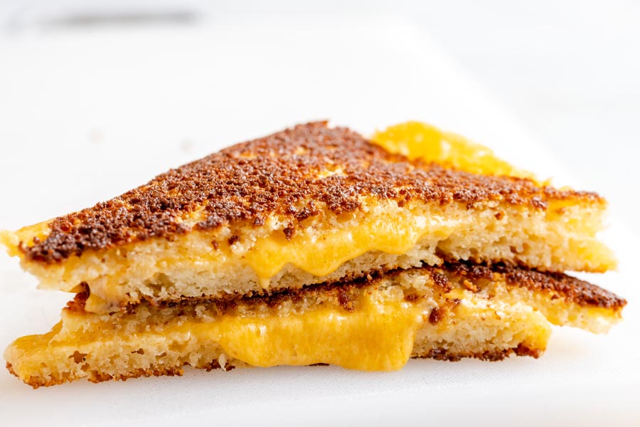 two sides of a grilled cheese sandwich stacked with cheese oozing out