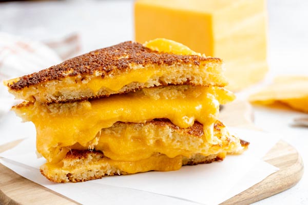cheddar cheese dripping down a stack of grilled cheese sandwiches sitting on parchment paper