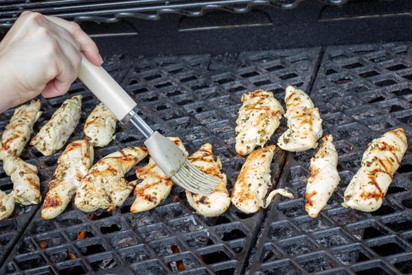 basting the chicken strips on a grill with a brown brush