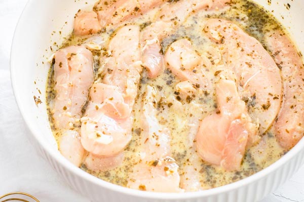 chicken sitting in a white bowl with herbs and spices in a wet marinade