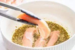 add raw chicken to a marinade in a white bowl