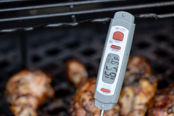 a meat thermometer stuck in a chicken leg that is on the grill