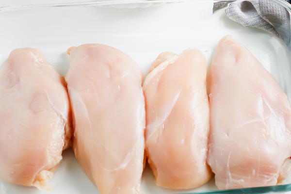 four chicken breast in a row on a cutting board