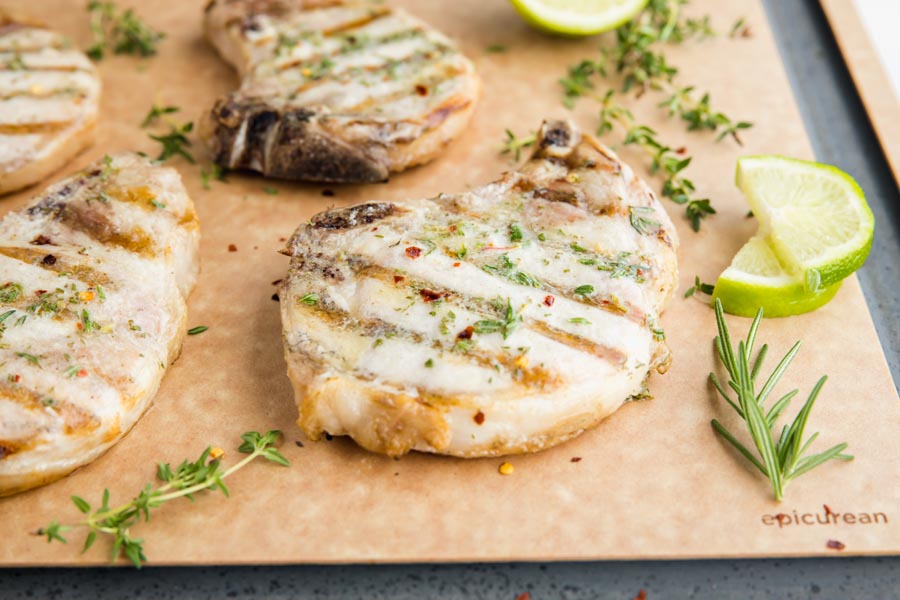 four grilled pork chops on a cutting board with rosemary and lime slices