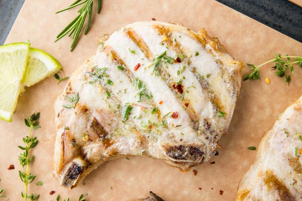 overhead shot of a grilled pork chop with limes and herbs near