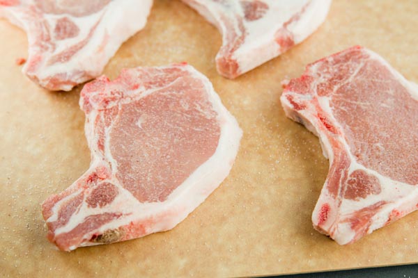 four bone-in pork chops on a wooden cutting board with black trim